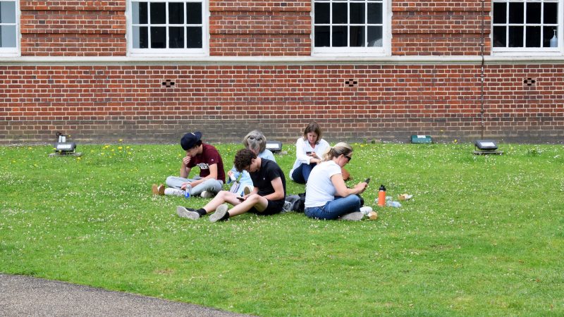 London, UK - Jul 15, 2024: Students and their parents check smartphones on the campus lawn
