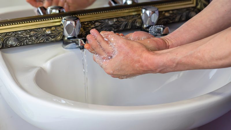 Hands being washed under taps.