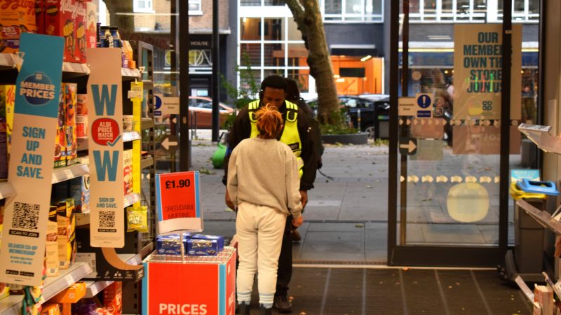 Security guard questions a regular female shoplifter carrying a bag of unpaid food