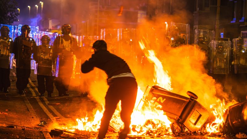 A rioter throws a brick at police during riots in Southport.