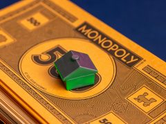 A stack of Monopoly money with a solo green house at the top.