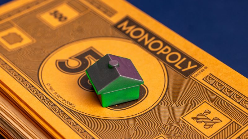 A stack of Monopoly money with a solo green house at the top.